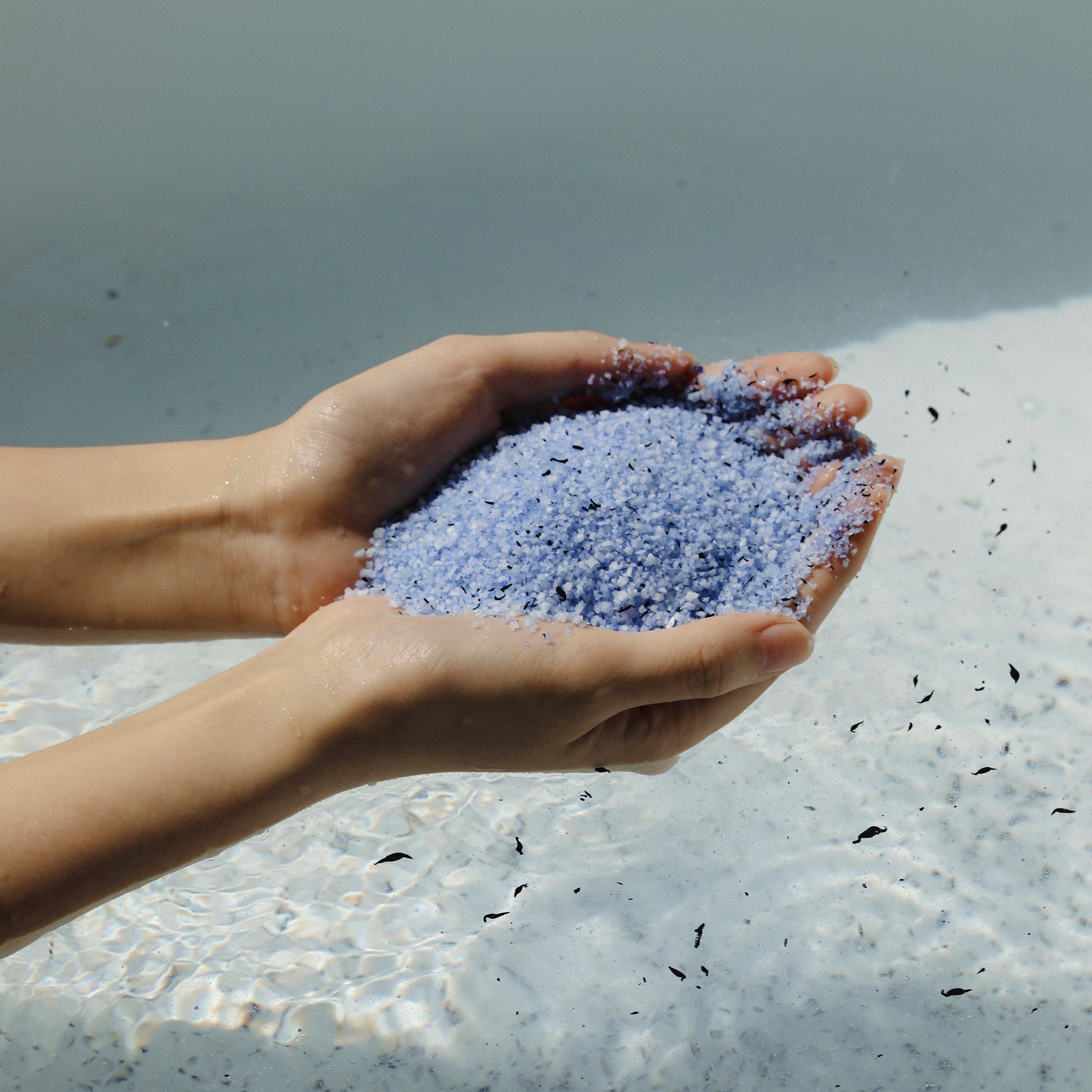 Two hands filled with ReSaltZ bath soak, held above a tub of water.