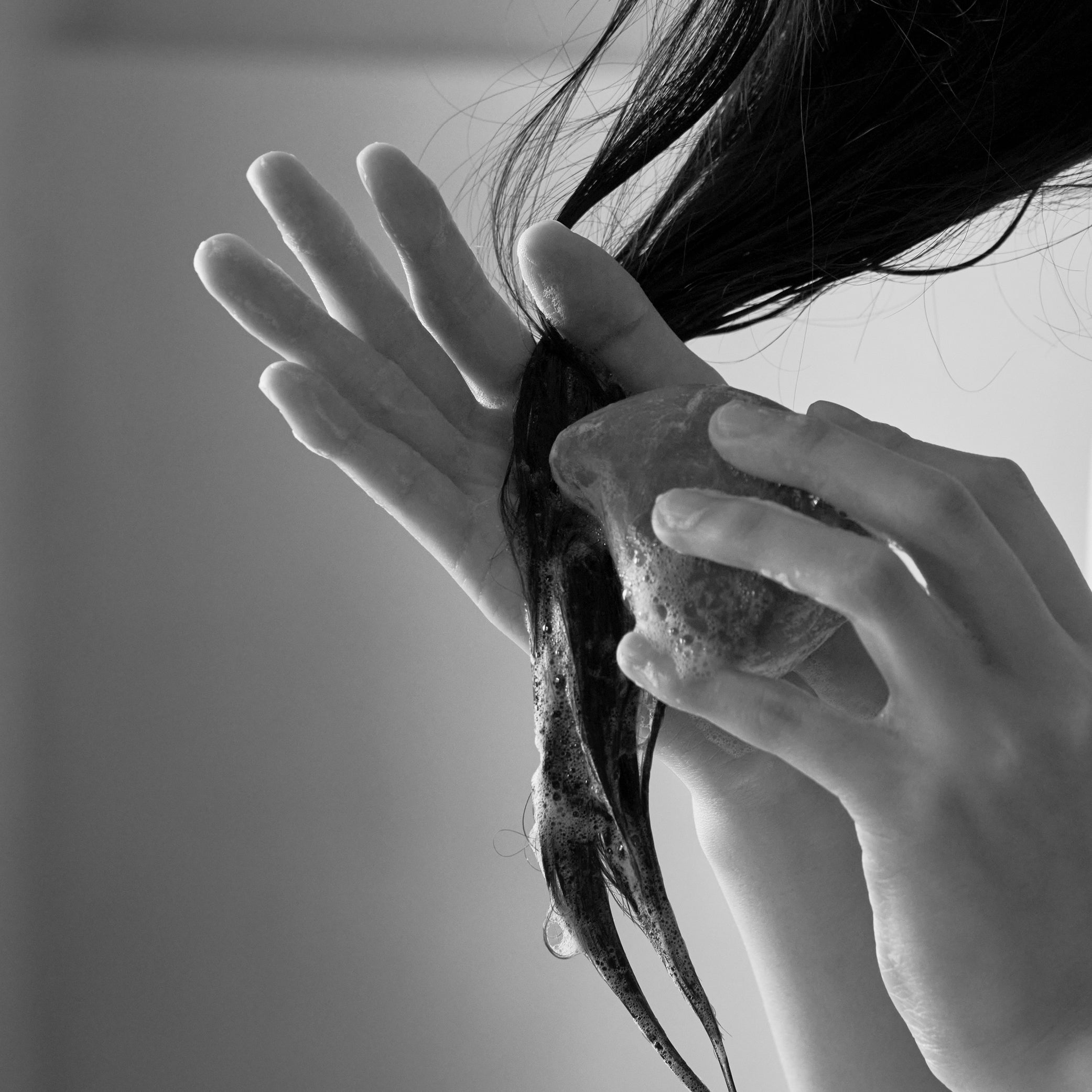 Person washing hair with Black Bean Shampoo Bar containing black beans, bamboo charcoal, and other scalp-friendly ingredients. The shampoo bar helps balance scalp oil and moisture levels, promoting healthy hair and scalp care