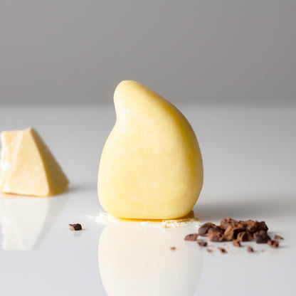Teardrop-shaped yellow hair conditioner bar made with natural organic oils. The product is designed to deeply nourish and condition hair, shown next to small pieces of ingredients.